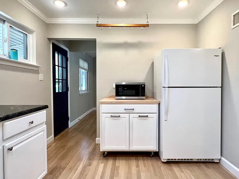 Hidden trash and recycling cans, microwave, refrigerator, hanging pan storage. Side door into carport; basement stairs across.