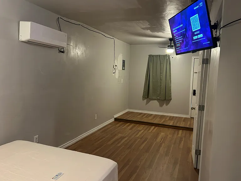 Private bedroom with wood-look flooring, wall-mounted A/C, and space for a bed and small desk or dresser.