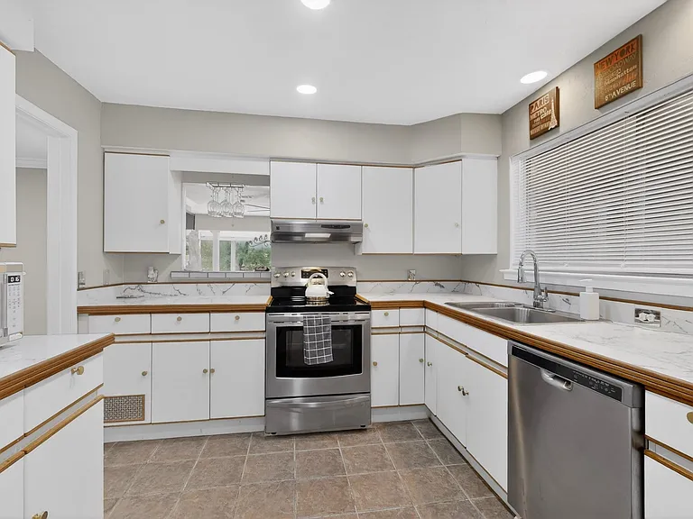 Bright kitchen with white cabinetry, dual sink, a wide window and sleek stainless steel appliances.
