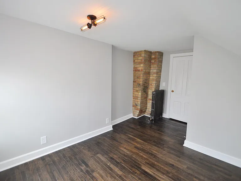 Medium bedroom with maple hardwood floors, exposed brick, new paint, and funky Edison bulb light fixture with dimmer switch