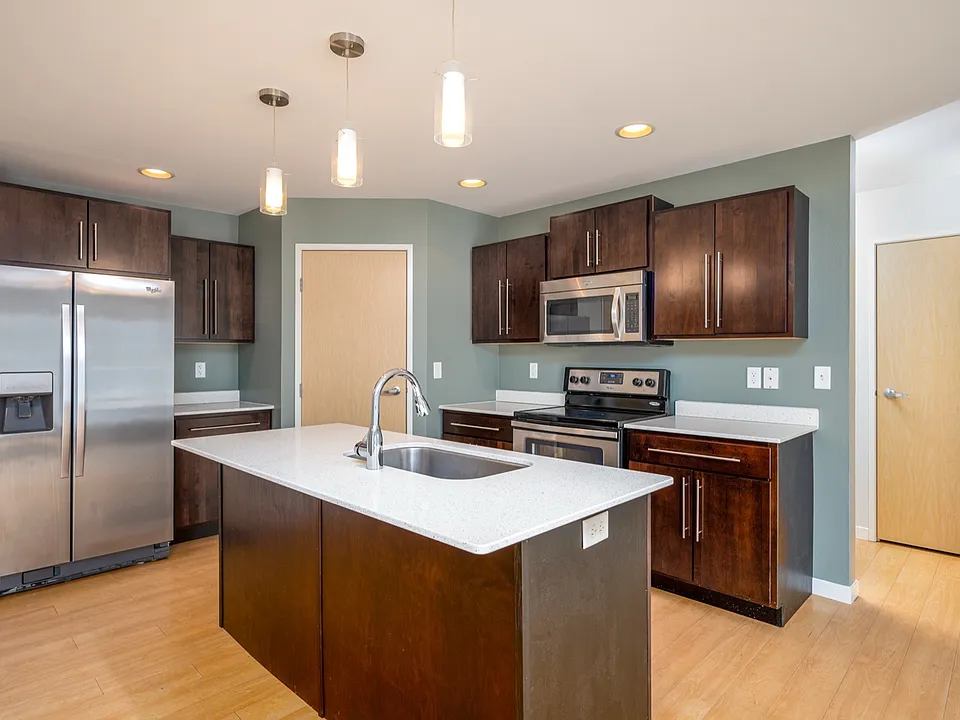 Modern kitchen with dark wood cabinets, sleek stainless steel appliances, and elegant pendant lighting over a spacious island. Modern kitchen with dark wood cabinets, sleek stainless steel appliances, and elegant pendant lighting over a spacious island.