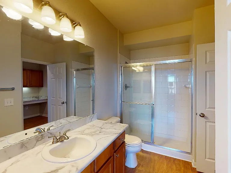Apartment bathroom with glass enclosed shower and wood-style flooring.