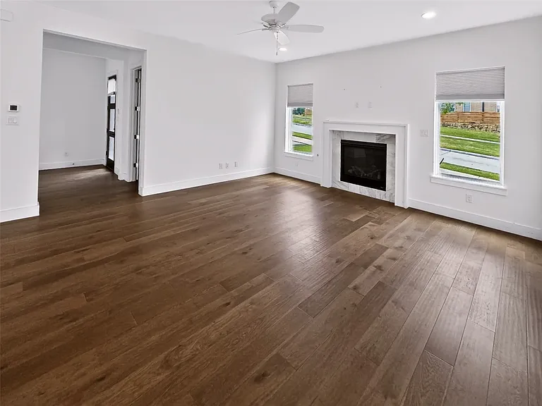 Spacious room featuring wood-finish flooring, a contemporary fireplace with a stone surround, recessed lighting, a ceiling fan, and multiple windows providing natural illumination