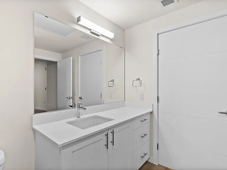 Sleek bathroom design featuring a wide quartz countertop, bright lighting, and modern shaker-style cabinetry. Sleek bathroom design featuring a wide quartz countertop, bright lighting, and modern shaker-style cabinetry.