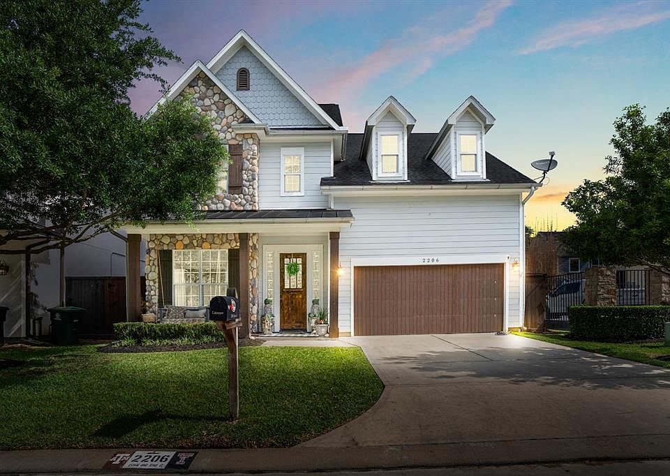 This Oak Forest area home greets guests with a covered porch, porch swing, stone accents, a metal roof and stained columns which match stained garage door.