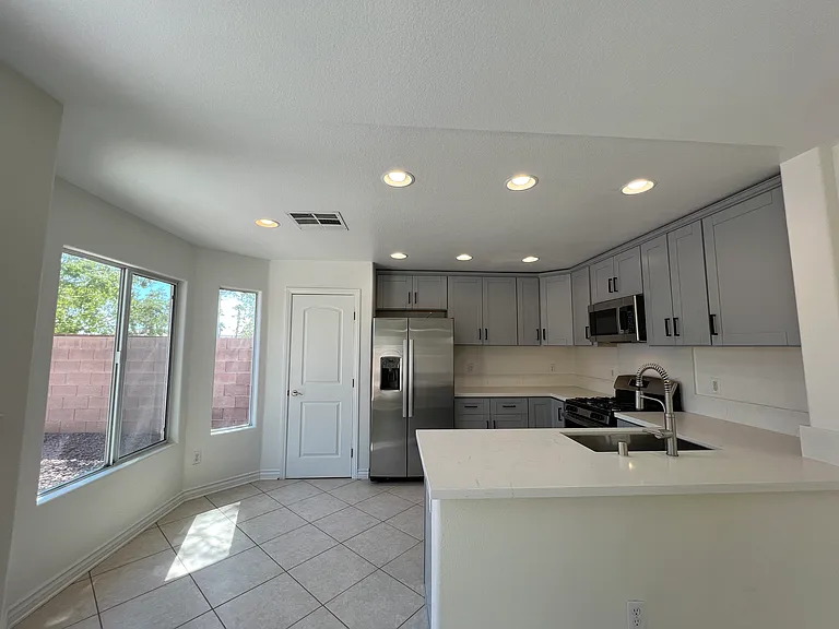 Remodeled kitchen with grey Shaker-style cabinetry, quartz counters, and stainless steel appliances. The bow window (on the left) accommodates a small breakfast nook.