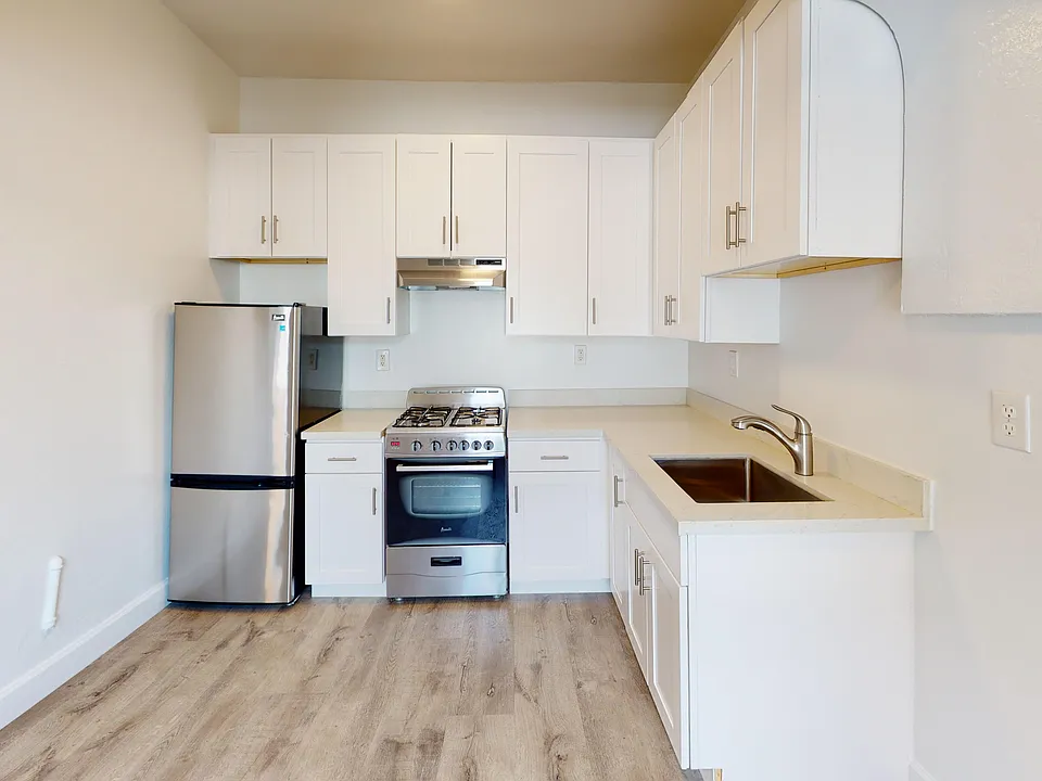 Kitchen with multiple cabinets, refrigerator, stove, range hood, and sink