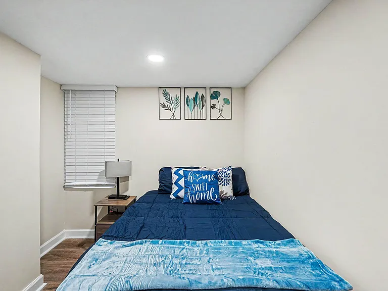 Furnished bedroom with a comfortable bed, nightstand with lamp, and window blinds for light control and privacy.