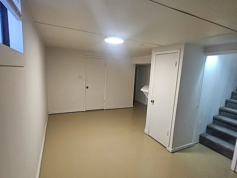 This is the additional study/living room downstairs. Door to the right is water heater. Door back left is a bedroom. Back right is the bathroom and another bedroom. To the right of the stairs is the laundry room. and a door going to the backyard.