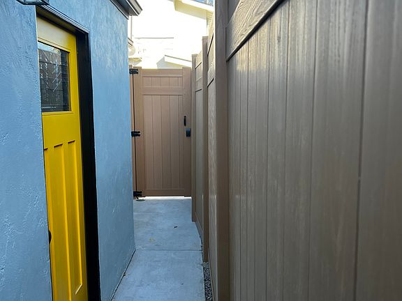 New privacy fence with secure gate. Front door and continued outdoor space. South wall, outdoor electrical sockets, light sensors, window to living area. Entry door with keyless entry.