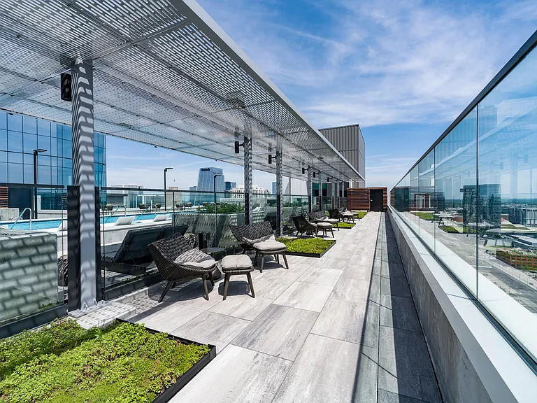 Rooftop promenade with shaded seating, planters, and glass railings offering relaxed lounge areas and expansive city views.