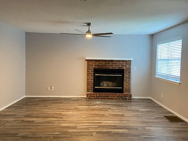Spacious, open living room with working fireplace featuring upgraded 60" ceiling fan, luxury vinyl tile flooring, soothing neutral grayish paint and new blinds.