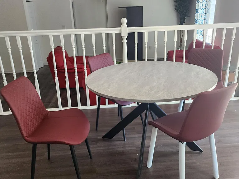 Open dining area with a round table and four chairs, overlooking a shared living space and nearby window seating.