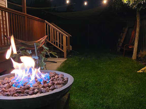 The backyard includes patio furniture, a propane fire table a wood firepit area, and stainless steel Weber Grill.