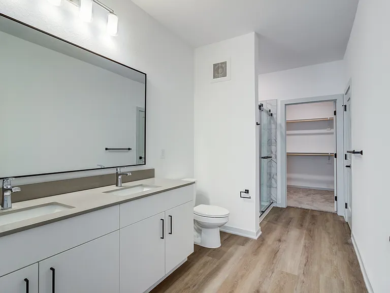 A double vanity with dual sinks, a large black-framed mirror, and a walk-in shower connect directly to the walk-in closet for a seamless, hotel-inspired suite experience.