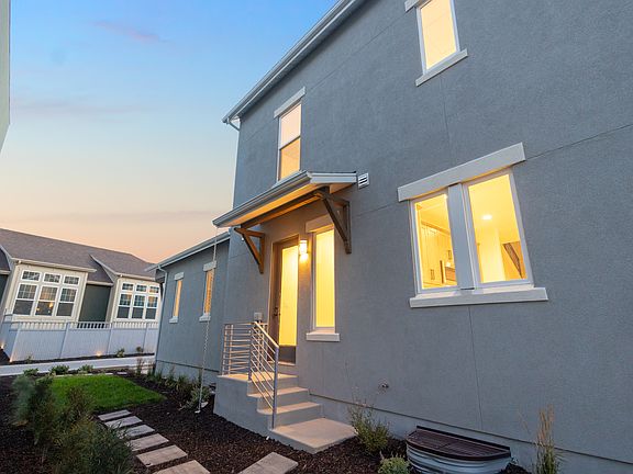 A modern gray two-story house from the Contempo Collection with lights glowing inside, a small entry