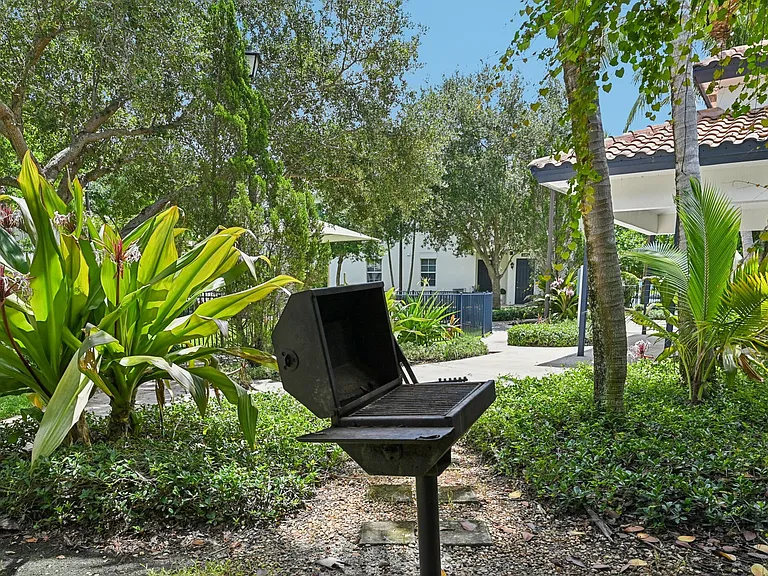 Outdoor patio featuring a barbecue grill surrounded by lush greenery and a cozy seating area.