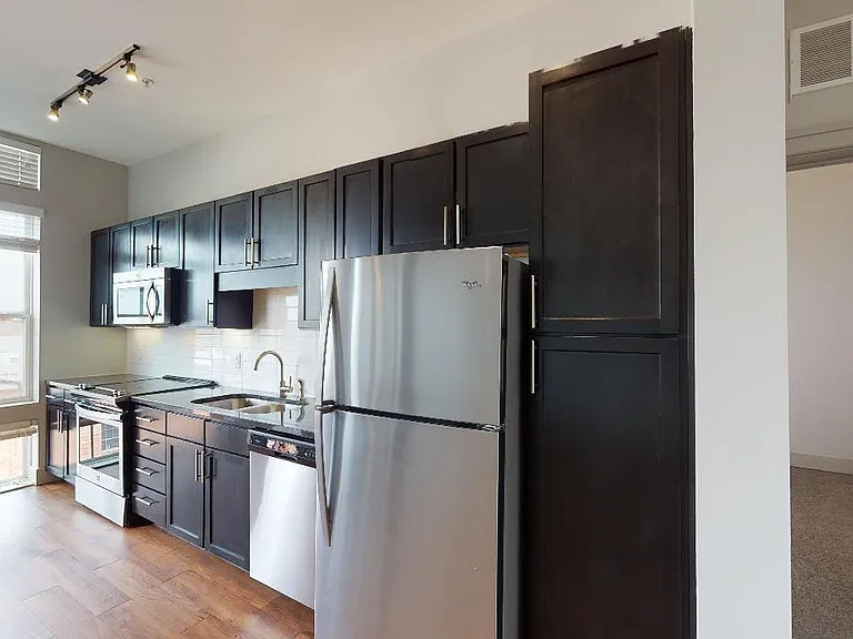 Apartment kitchen with stainless steel appliances, granite countertops and wood-style flooring.