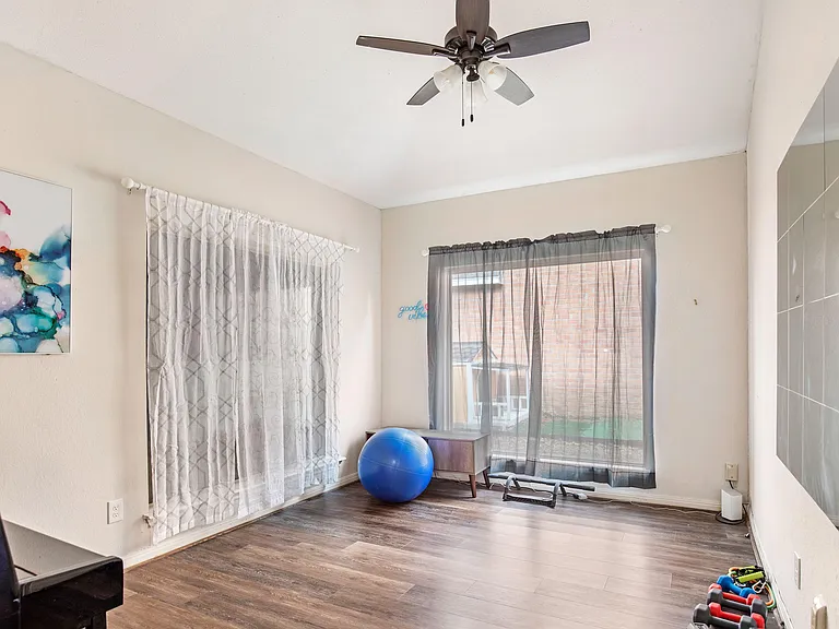 Open living area with wood-style flooring, ceiling fan, and large windows with curtains for comfortable everyday use.