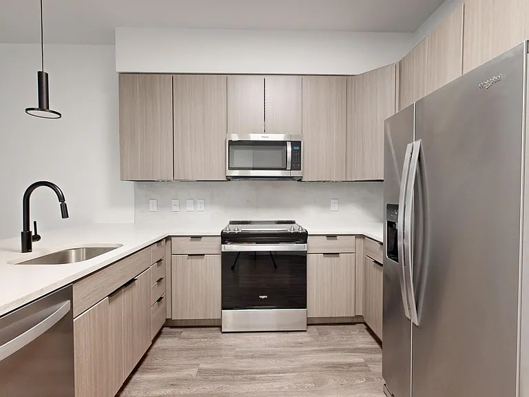 Apartment kitchen with stainless steel appliances, quartz countertops, and wood-style flooring.