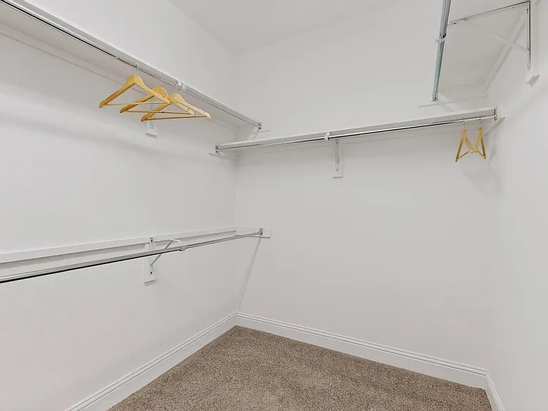 A spacious walk-in closet featuring white walls and neatly arranged shelves