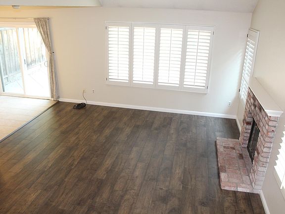 `Large living space with wood laminate floors, plantation shutters, wood burning fire place, and vaulted ceilings.