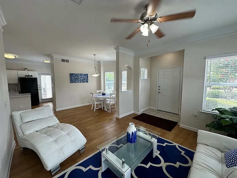 Bright and inviting living room with elegant composite wood floors, modern white furniture, and a chic dining area adjacent to the kitchen. Bright and inviting living room with elegant composite wood floors, modern white furniture, and a chic dining area
