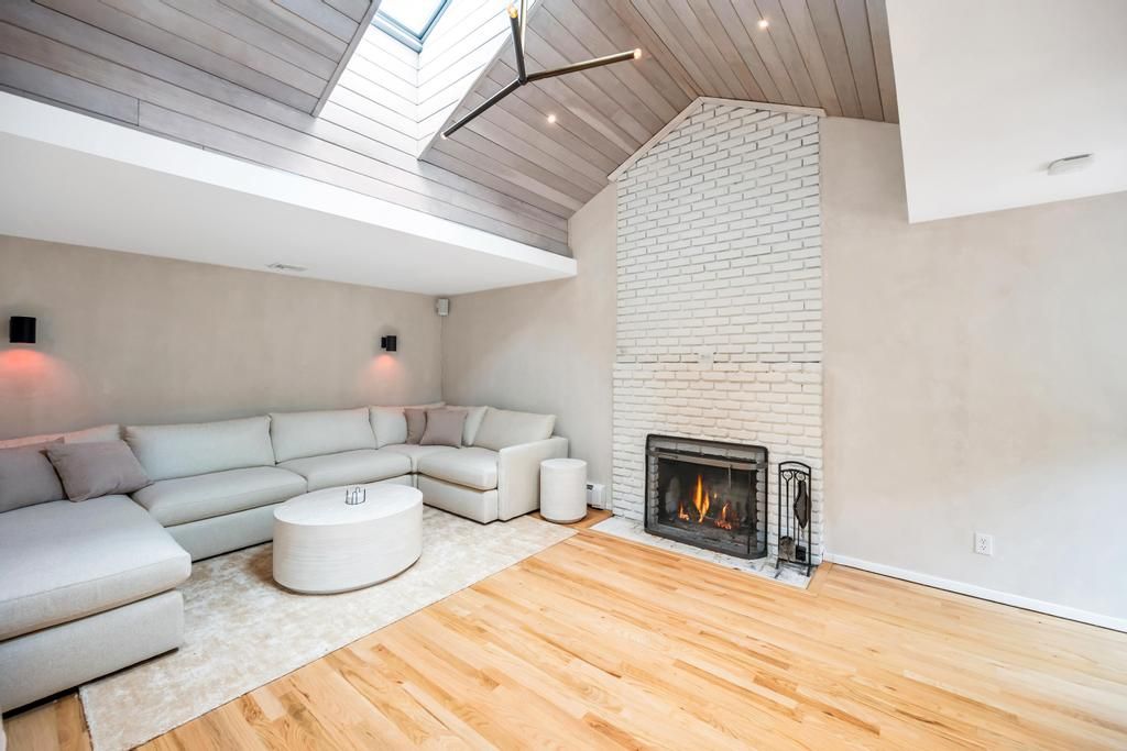  Spacious Living room with high ceilings, skylights, large couch, tv, and fireplace.