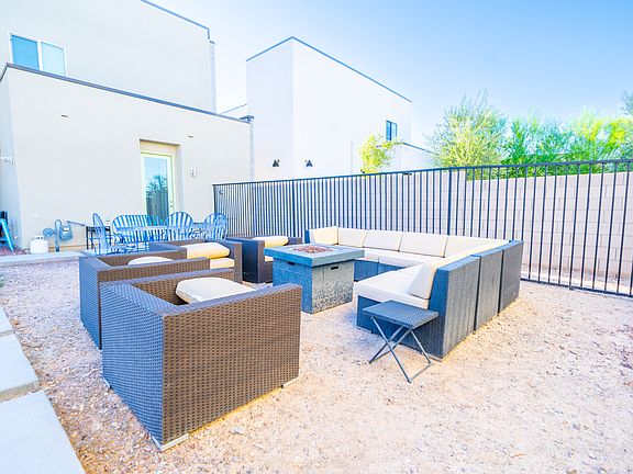 The image features a cozy outdoor seating area with modern furniture, including a sectional sofa and a fire pit, enclosed by a fence for privacy.