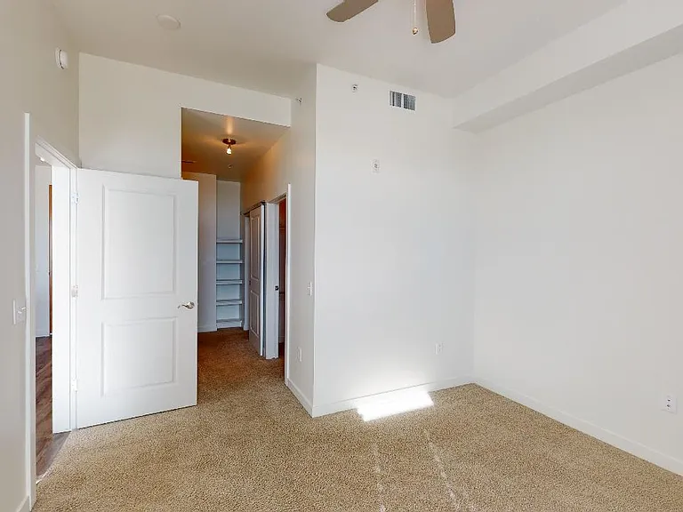 Spacious apartment bedroom with large closet, attached bathroom and plush carpet flooring.