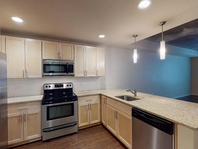 Apartment kitchen with stainless steel appliances, granite countertops and wood-style flooring.