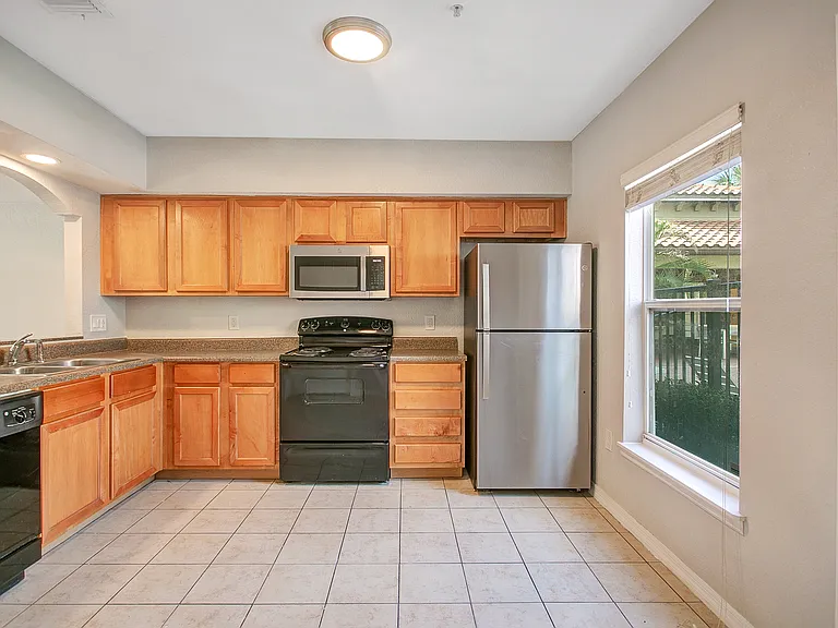 apartment kitchen featuring wooden cabinets, tile flooring, dishwasher, range, microwave, and stainless steel refrigerator