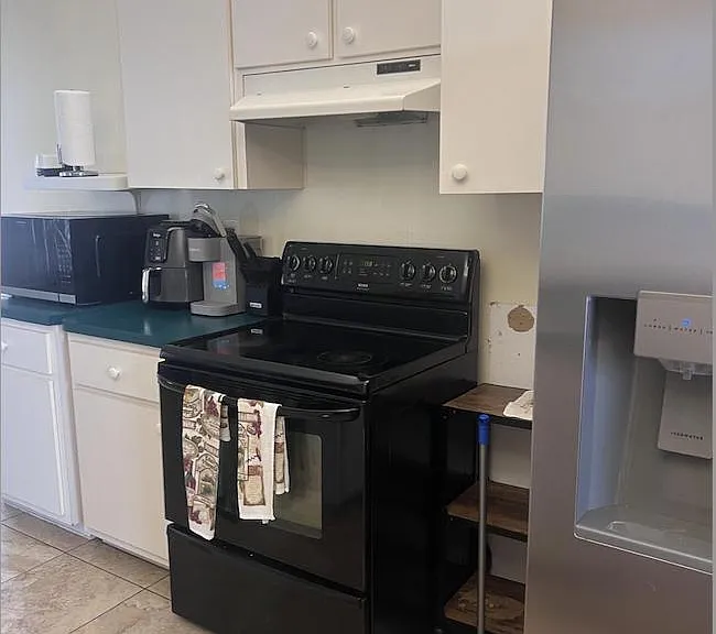 Functional kitchen setup with ample white cabinetry, electric range, and a full-size refrigerator with in-door water/ice.
