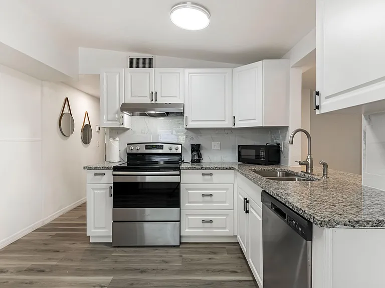 Efficient galley kitchen with ample white cabinetry, granite-look counters, and stainless range, dishwasher, and sink.