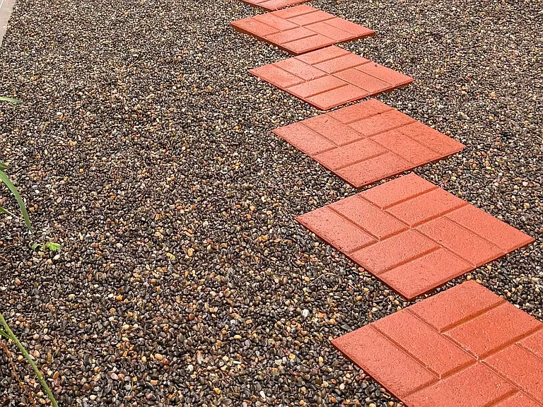 Beautiful walkway featuring red pavers set over pea_sized river rock, artificial grass turf, creating a playful and textured path where kids love to spend hours exploring and enjoying the outdoors.