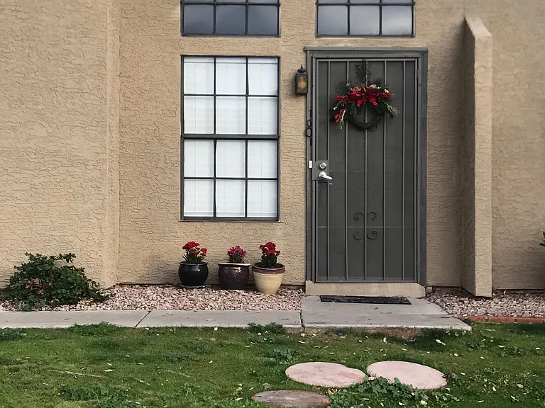 Inviting front entry with a secure metal door, large windows, and low-maintenance landscaping with potted plants.