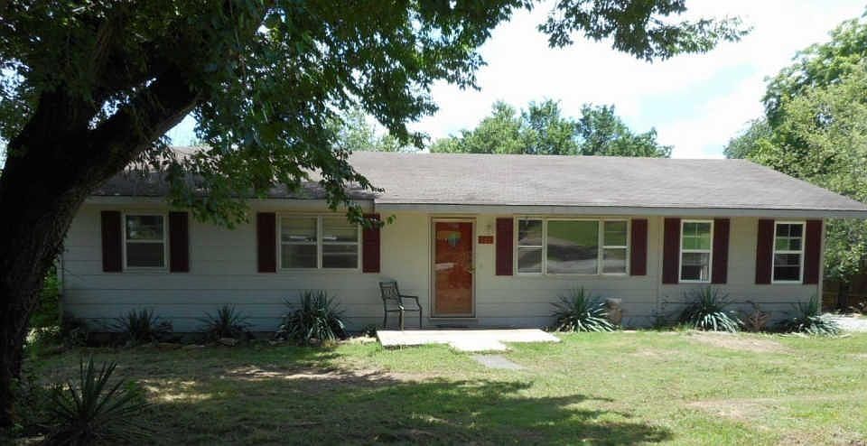 Front of house with manicured lawn and trees.