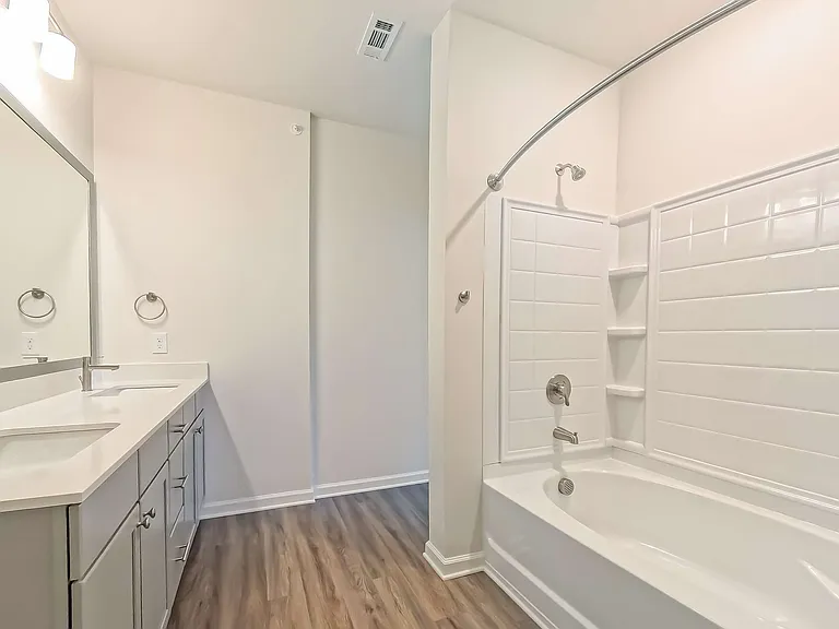 Modern bathroom featuring sleek double sinks, elegant mirror, and a pristine tiled bathtub, complemented by warm wooden flooring.