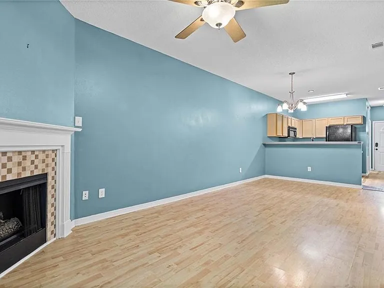 Living area featuring wood-finish flooring, a fireplace with a tiled surround, a ceiling fan, and an open layout to a kitchen area with wood cabinetry and black appliances