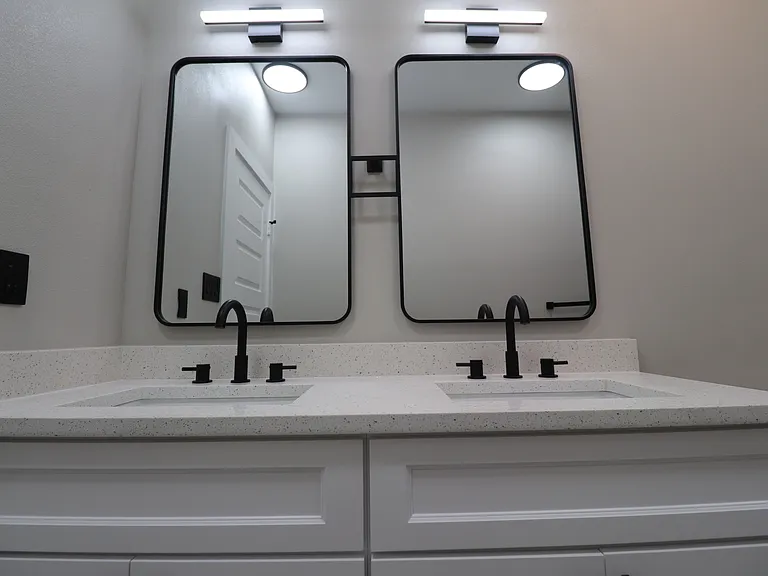 Modern double vanity with two illuminated mirrors, black hardware, and plenty of cabinet storage.