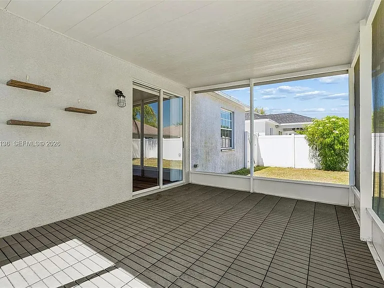 Screened-in patio with tile flooring and sliding glass doors, opening to a fenced backyard for outdoor lounging.