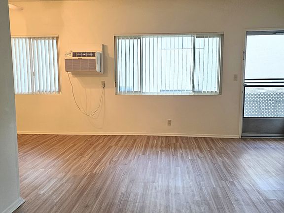 View of the Living room with 2 windows, front door, wall air conditioner with remote control!