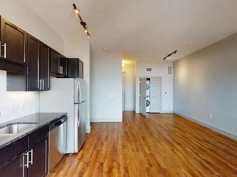 Apartment kitchen with stainless steel appliances, dining and living room with wood-style flooring.