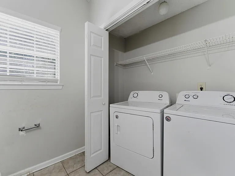 Dedicated laundry room with full-size washer and dryer, tile flooring, and wall shelving for convenient storage.