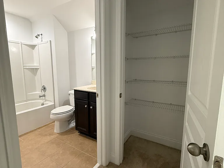 Convenient upstairs full bathroom featuring a tub/shower combo, dark vanity cabinetry, and a dedicated, spacious linen closet right outside the door."