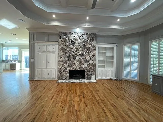 Unfurnished living room featuring a stone fireplace, light wood-style floors, crown molding, recessed lighting, and beam ceiling