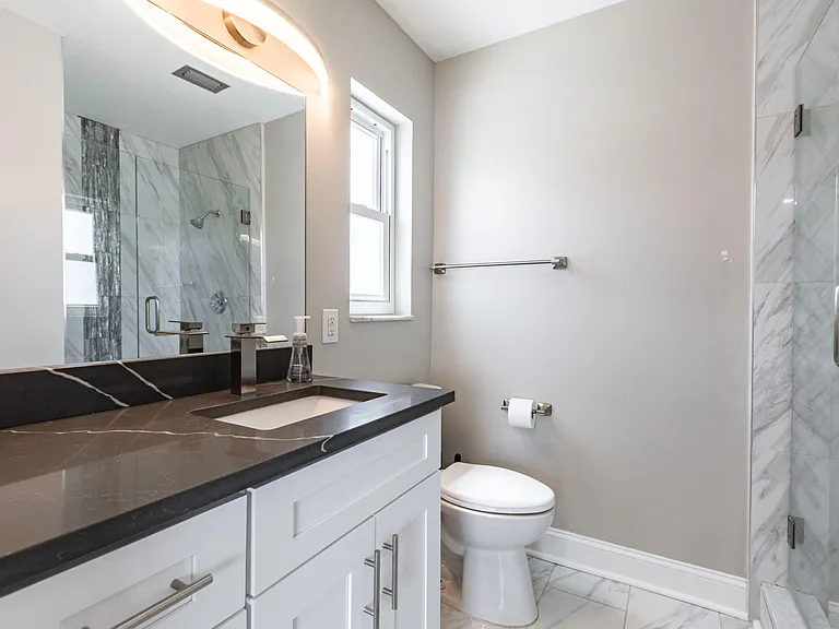 Updated bathroom with a stone-look vanity, large mirror, window, and glass-enclosed shower with tile surround.