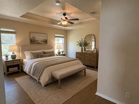 AI decorated Master bedroom with pop-up ceiling and ceiling fan. Nice view of wooded area behind house.