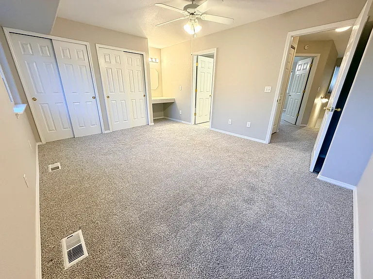 Spacious primary bedroom with double closets and a built-in vanity area featuring an oversized countertop, dedicated mirror, and vanity lighting.