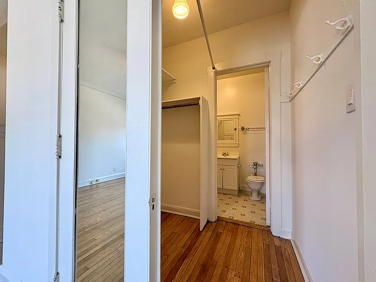 Bright hallway leading to a cozy bathroom with elegant hardwood flooring and a spacious mirror. Bright hallway leading to a cozy bathroom with elegant hardwood flooring and a spacious mirror.